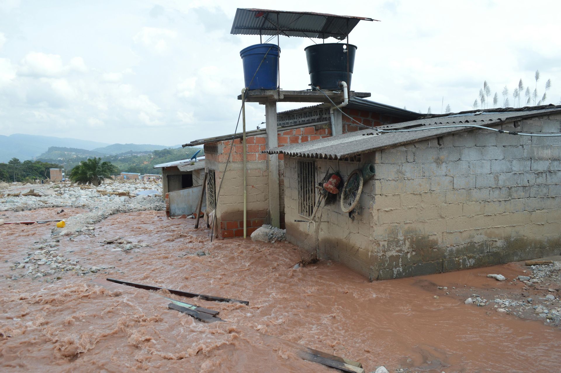 A brick building with two blue buckets on top of it in a flooded area.