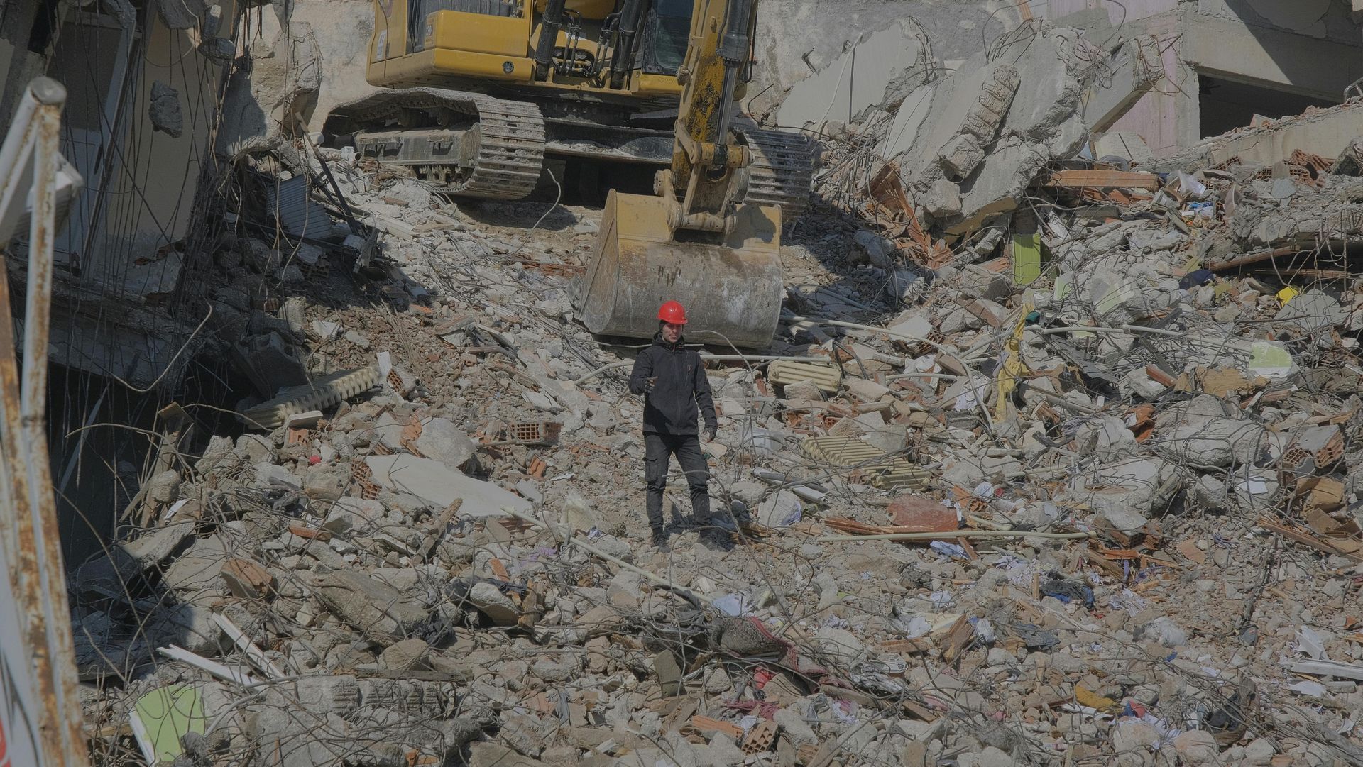 A man is standing in a pile of rubble next to a bulldozer.