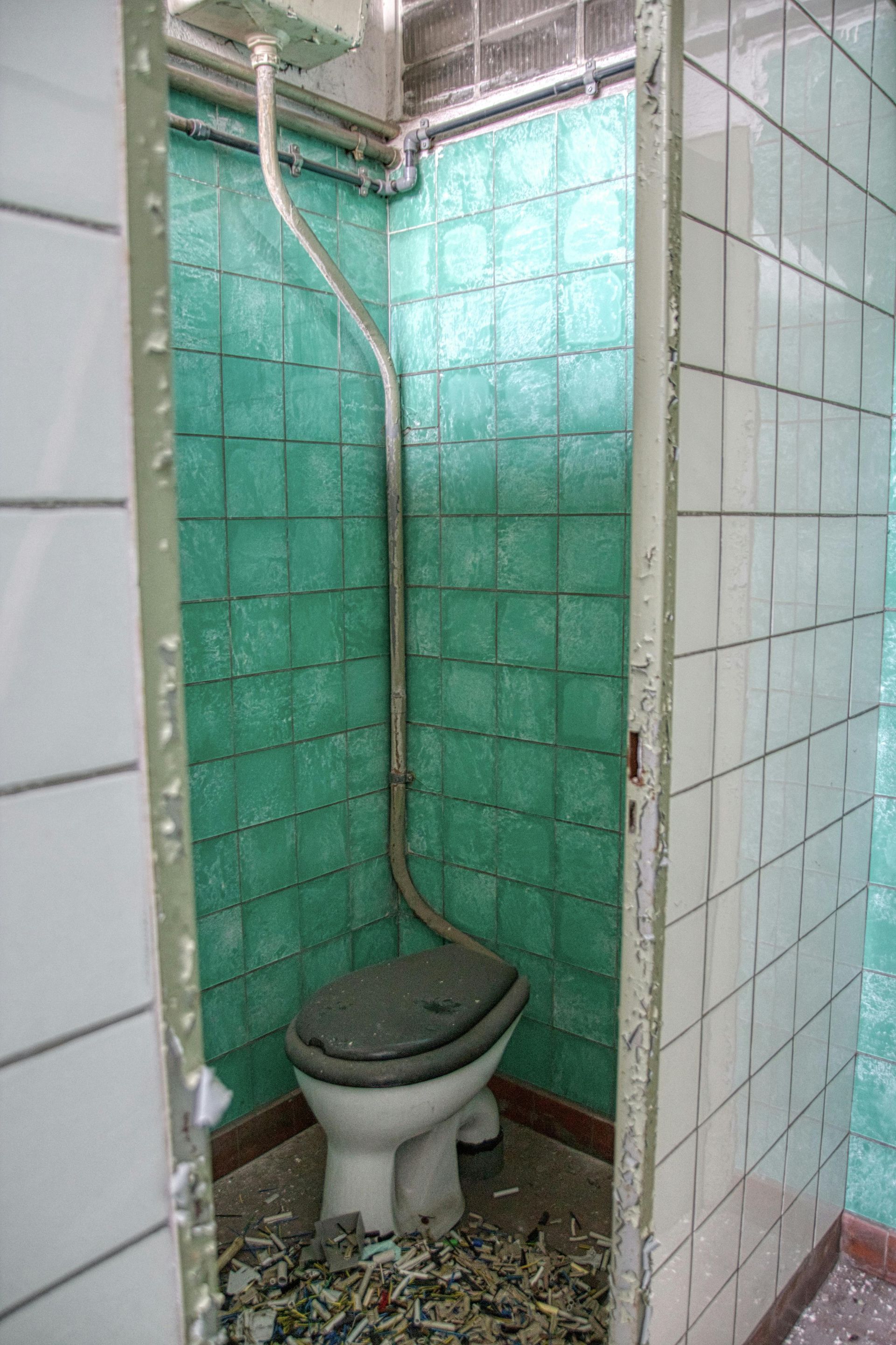 A toilet is sitting in a bathroom with green tiles.