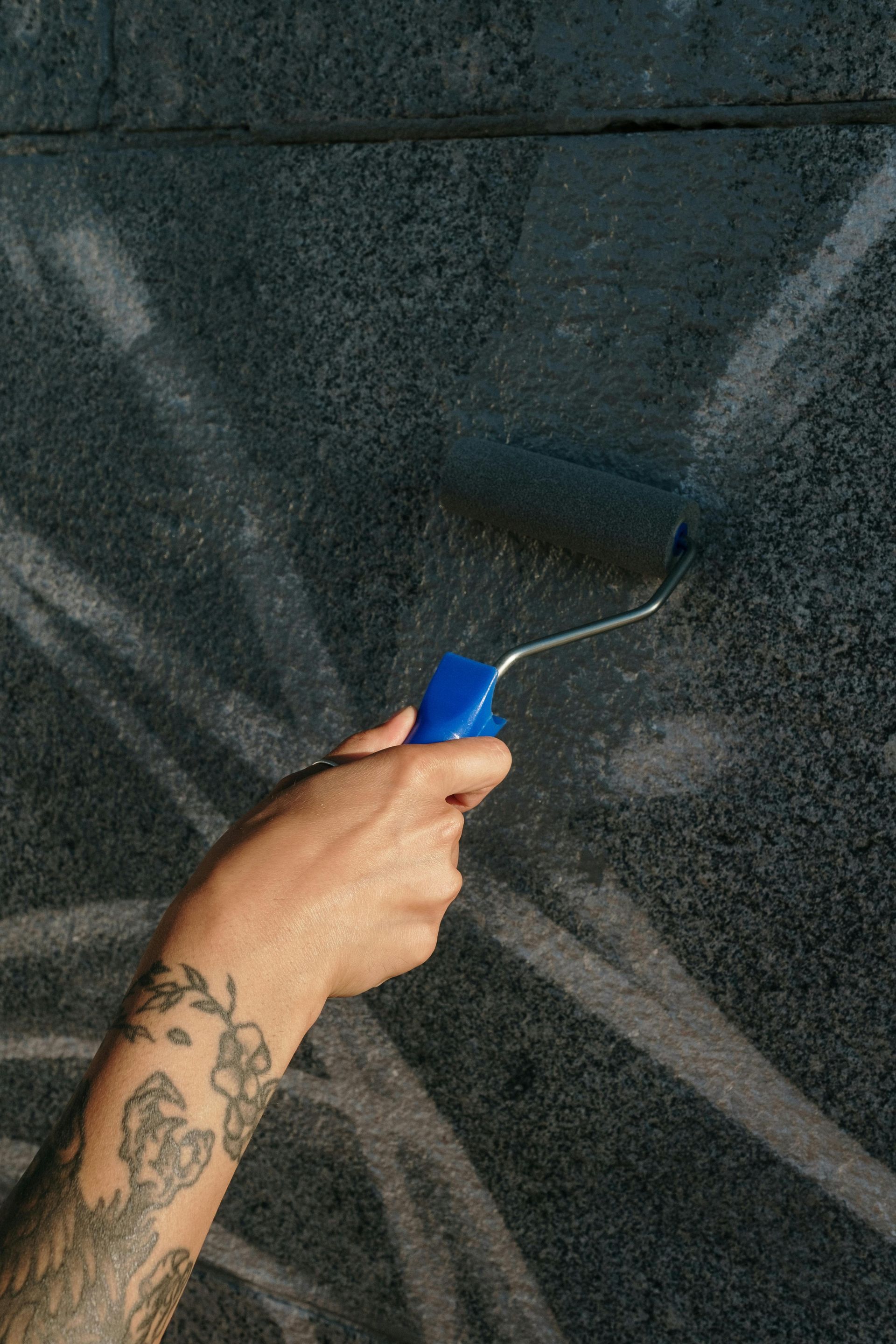 A person with tattoos is painting a wall with a roller.