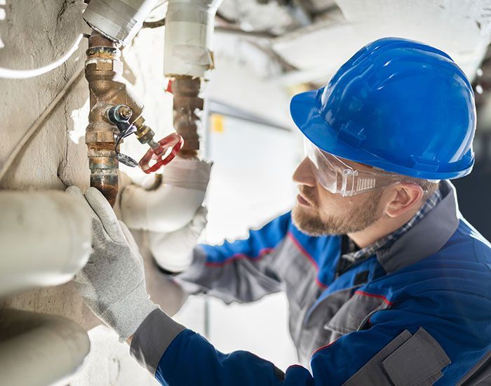 A man wearing a hard hat and safety glasses is working on a pipe. — Elgin, IL — All Suburban Emergency Plumbing