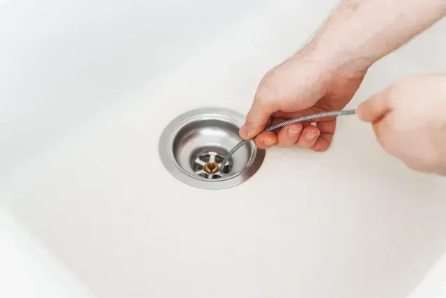 A person is cleaning a sink drain with a spoon. — Elgin, IL — All Suburban Emergency Plumbing A person is cleaning a sink drain with a spoon. — Elgin, IL — All Suburban Emergency Plumbing
