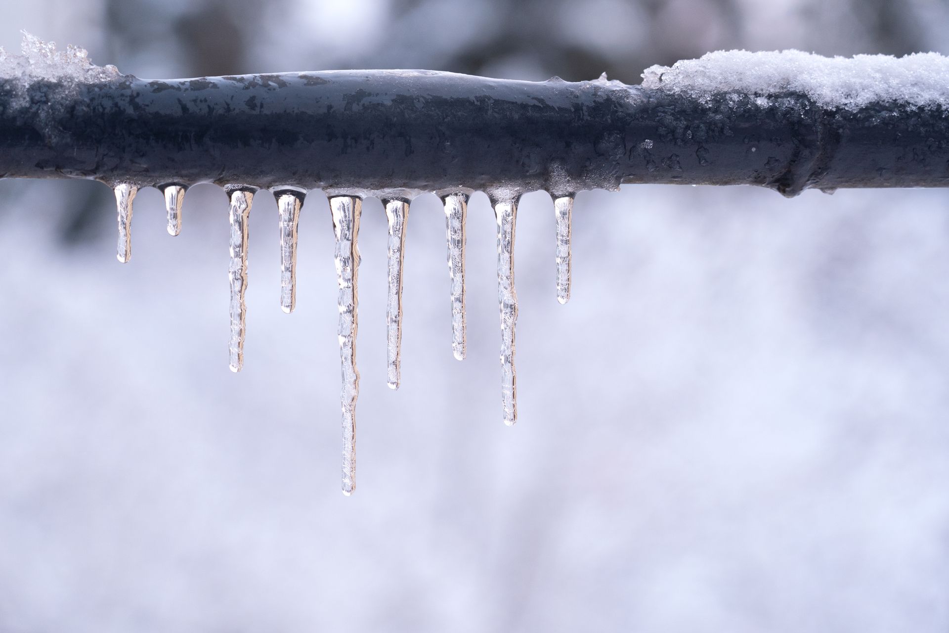 Frozen icicles on a gray pipe, showcasing the need of expert plumber services.