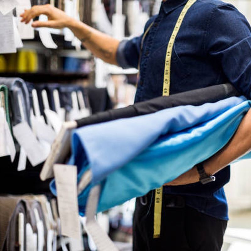 Tailor holding fabric rolls, reaching for a tag, in a fabric store.