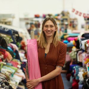 Woman holding a roll of pink fabric in a fabric store, smiling.