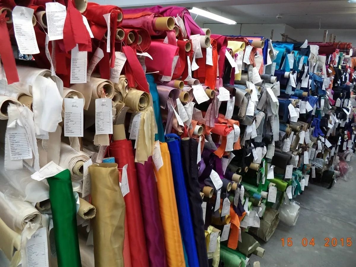 Rows of colorful fabric rolls with attached tags in a warehouse setting.