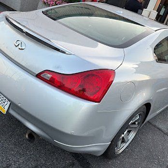 Silver Infiniti G37 coupe. Rear view, showing taillight, spoiler, and exhaust. Parked on asphalt.
