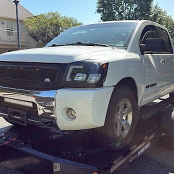 White Nissan Titan truck on a trailer, with a black grille and custom headlights.