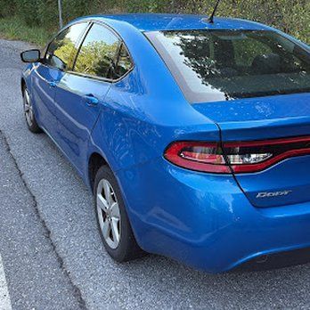 Blue Dodge Dart parked on the side of a road, with sunlight reflecting off the car.