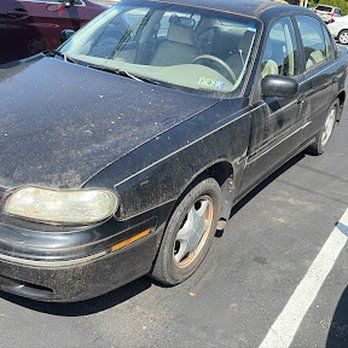Black, dirty Chevy Malibu sedan parked in a parking lot on a sunny day.