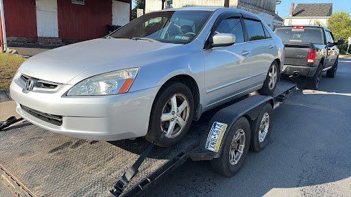 Silver Honda Accord on a trailer being towed by a black pickup truck on a paved road.