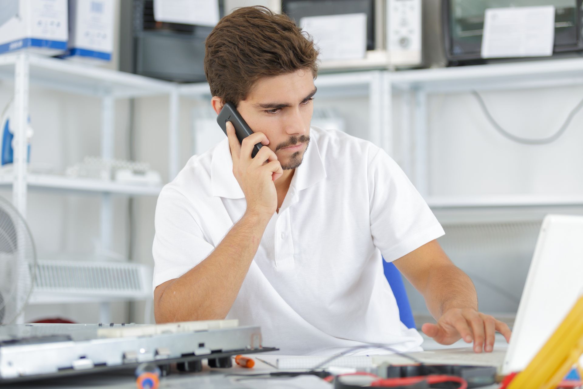 A technician using his mobile phone and checking on a repaired laptop at a workshop.