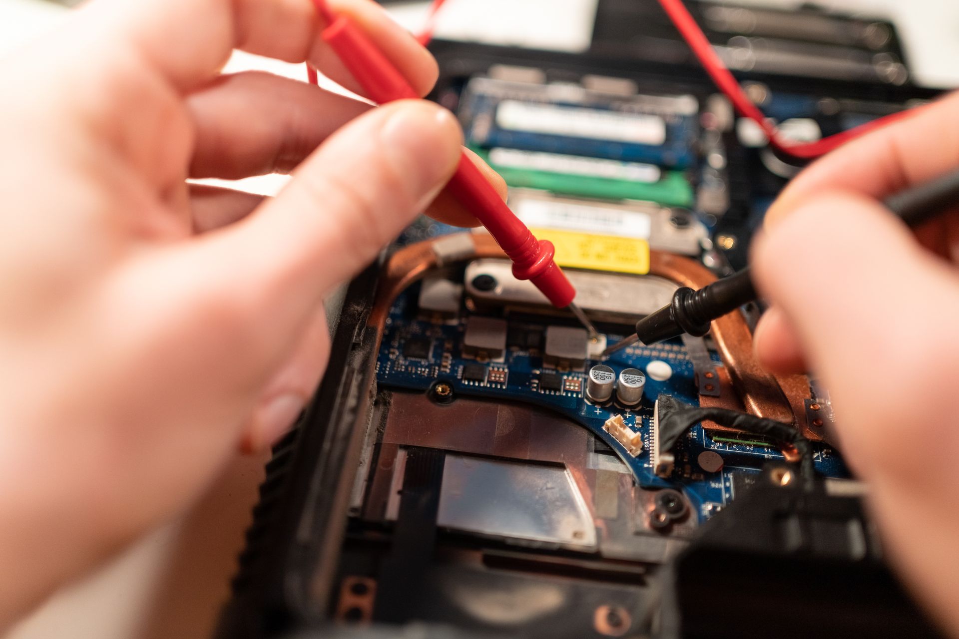 A close-up of a technician checking the hard drive on a computer with a multimeter.