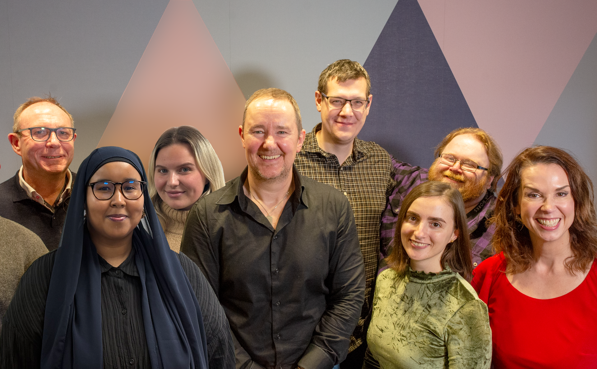 Group of people smiling, posing in front of a patterned wall.