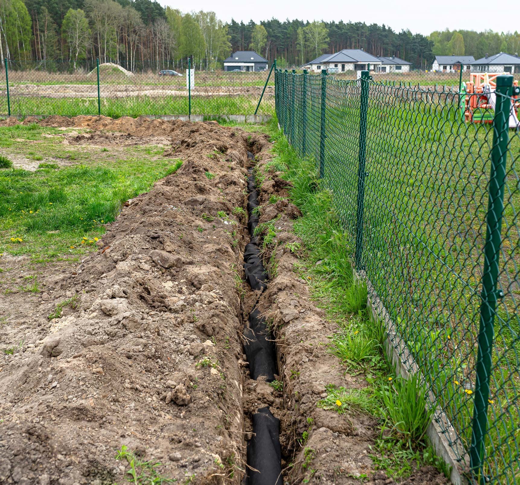 A trench dug in the yard along the fence to lay the drainage pipe.