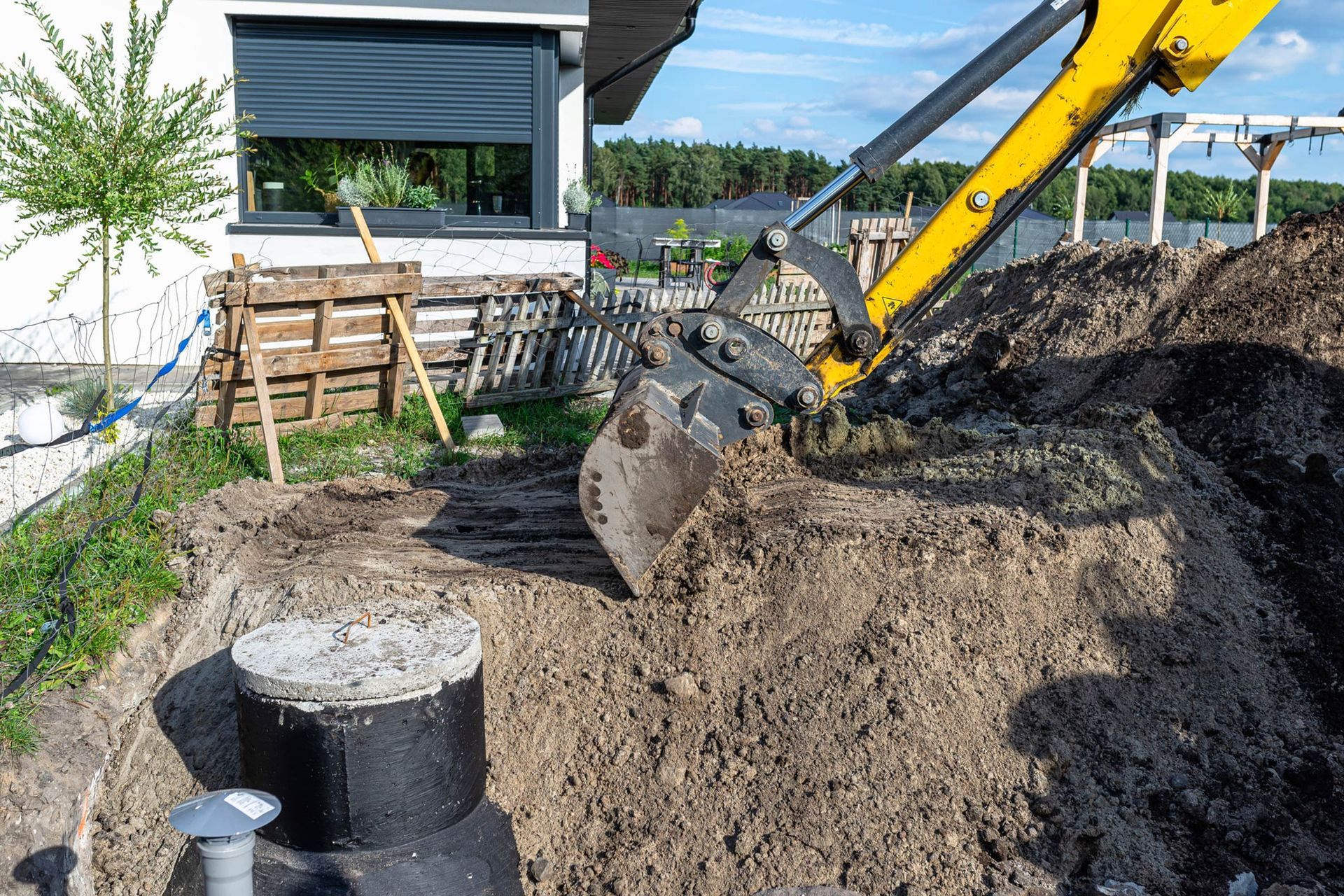 A yellow excavator is digging a hole in the ground in front of a house.