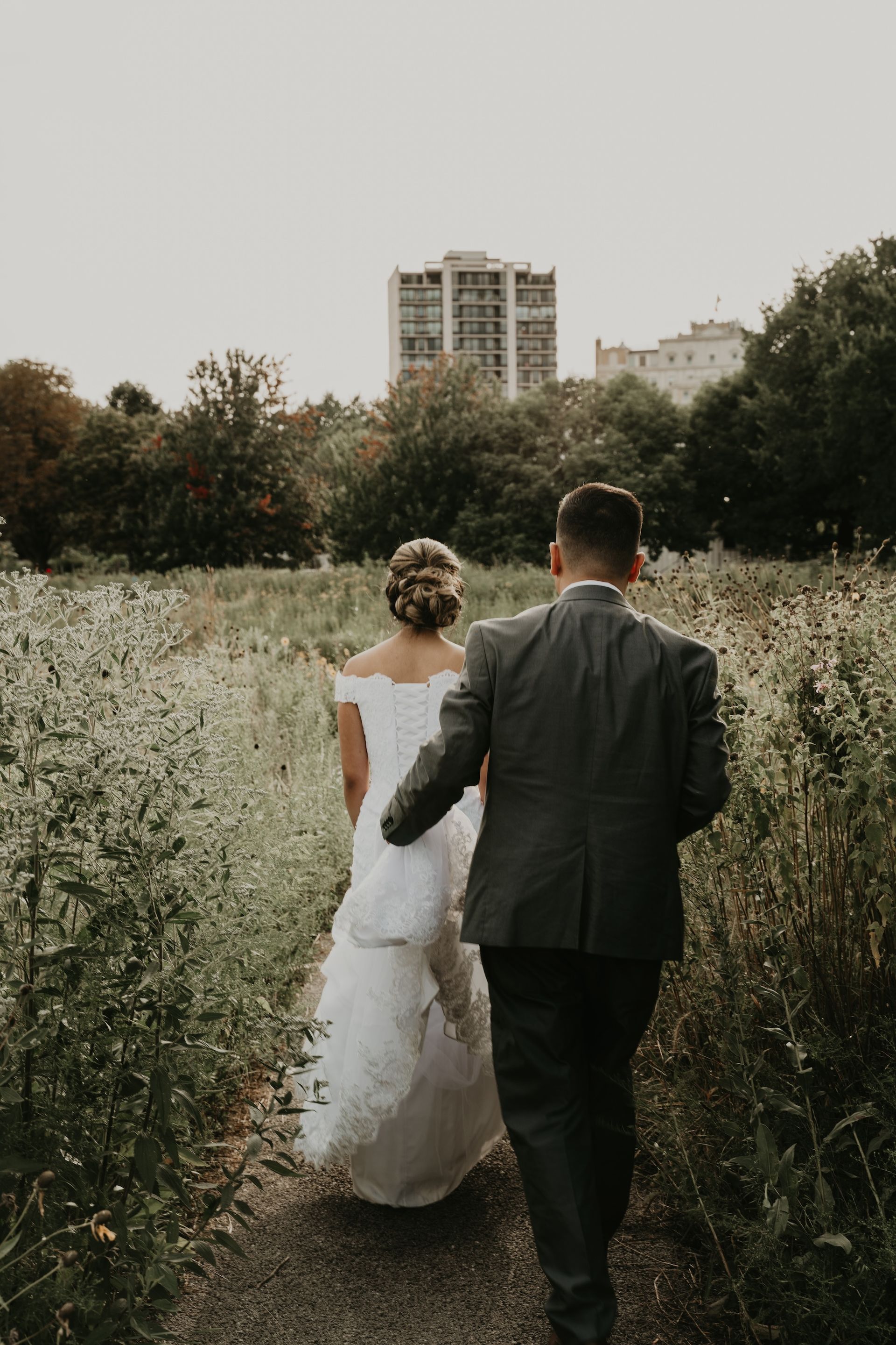 A bride and groom are walking down a path in a field.