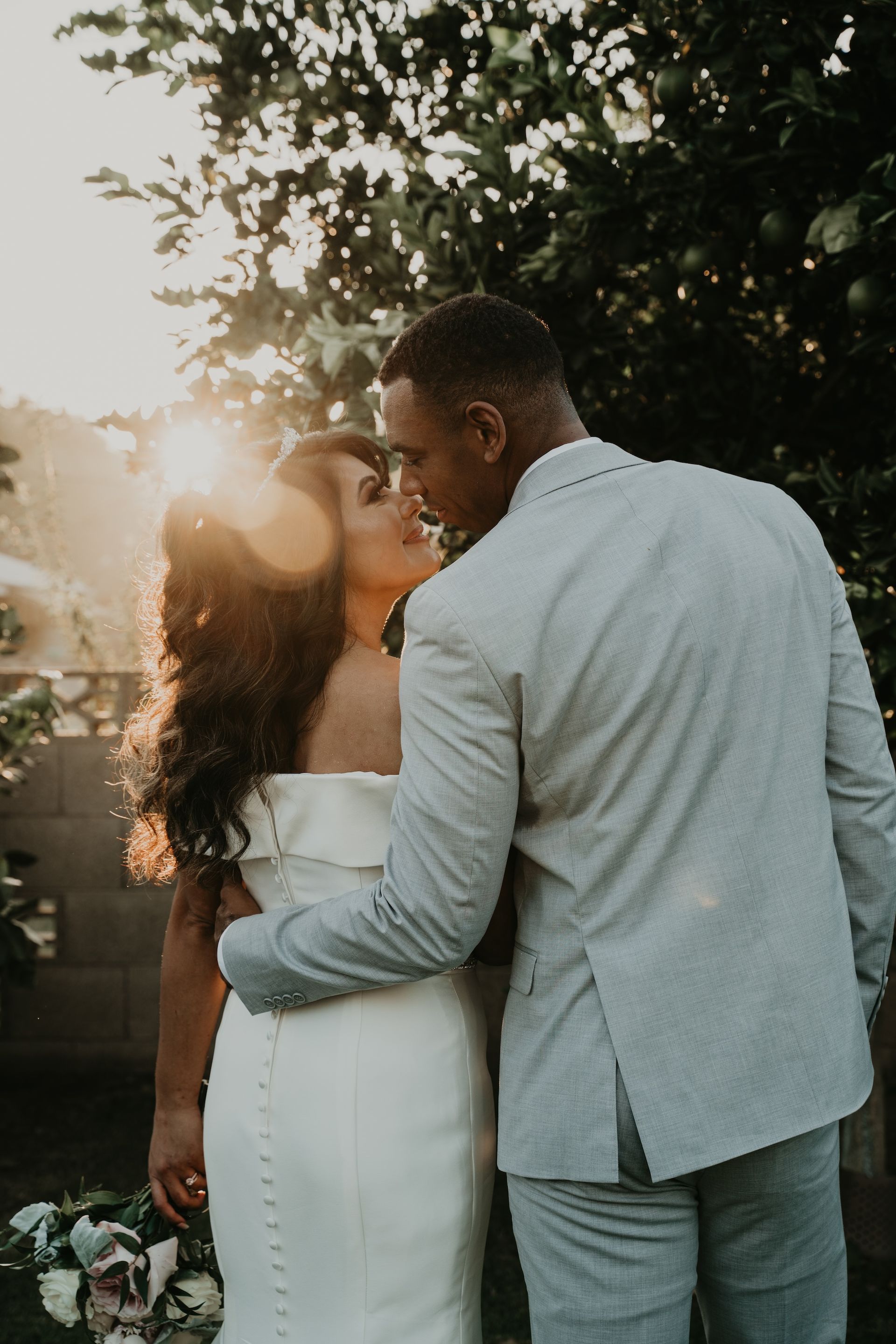 A bride and groom are kissing in front of a tree.