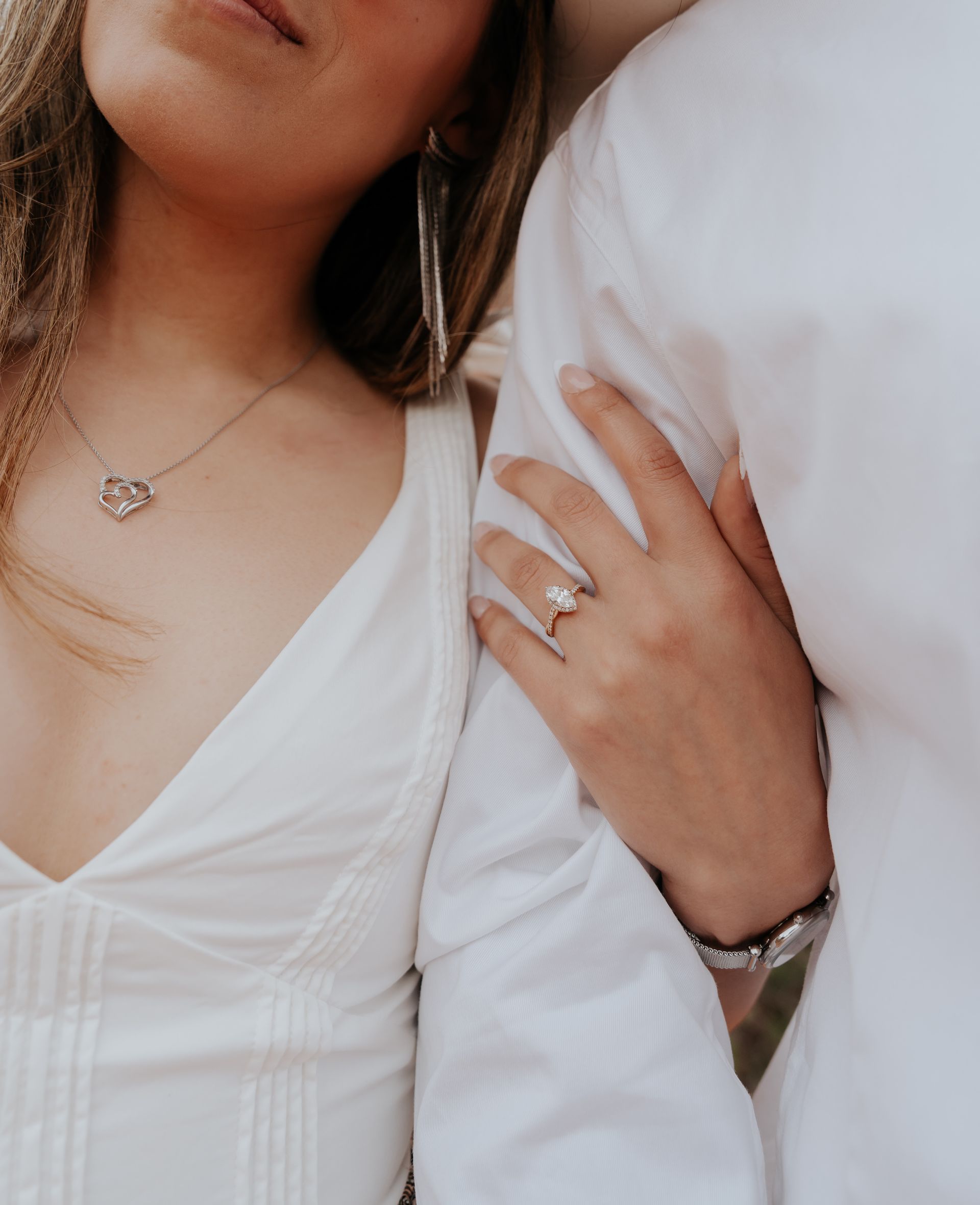 A woman wearing a necklace and a ring is holding a man 's arm.