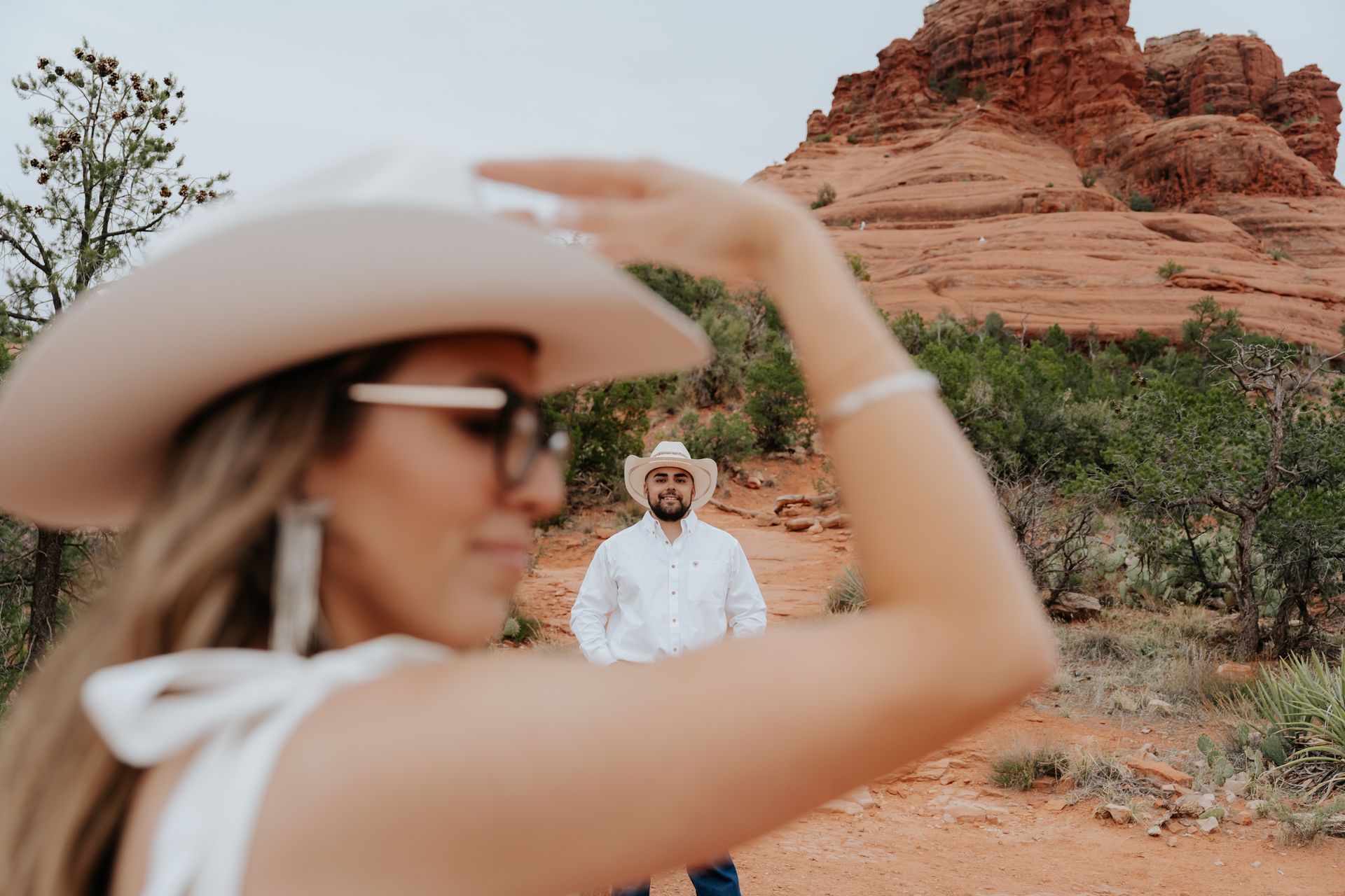 A woman in a cowboy hat is taking a picture of a man in the desert.