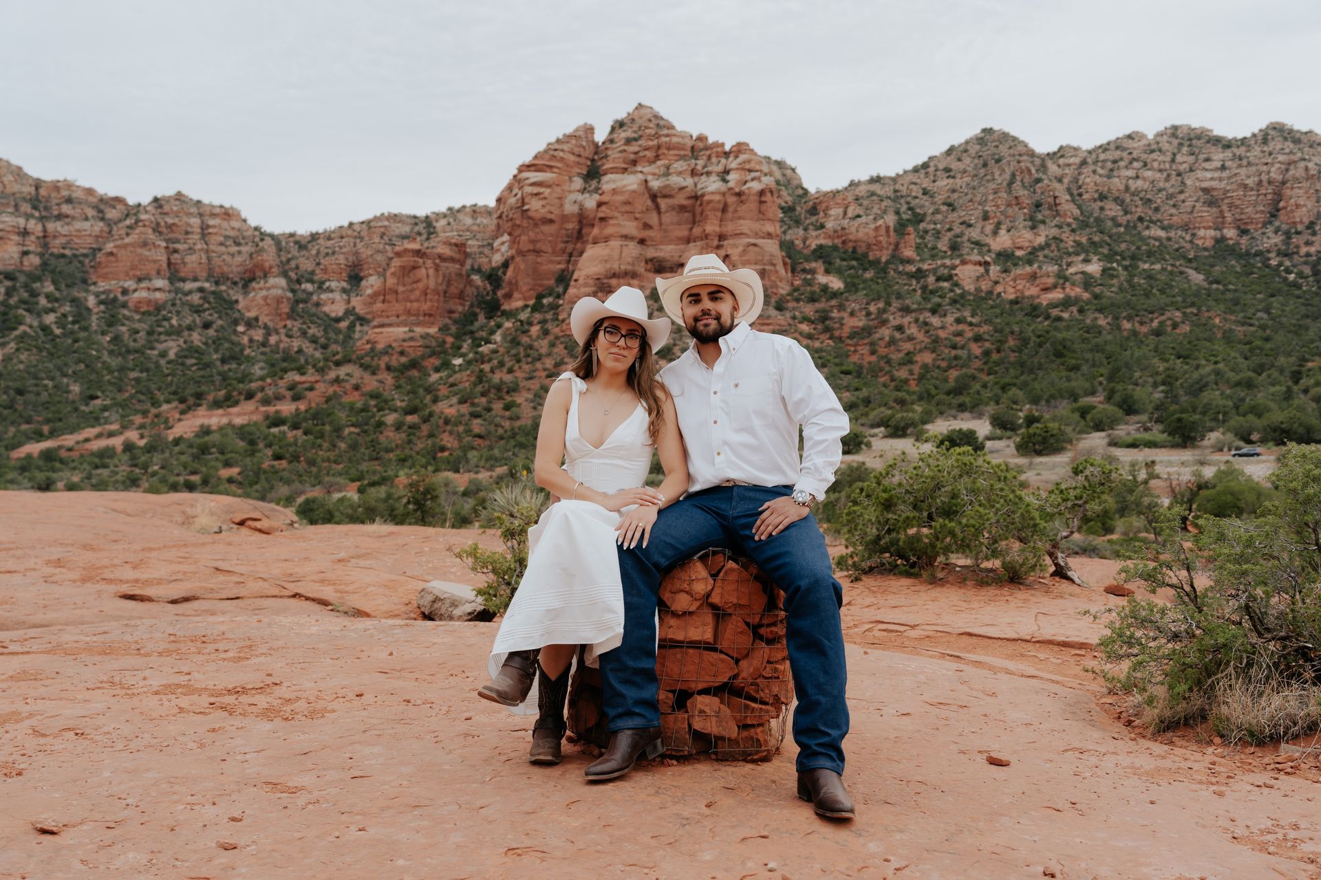 A bride and groom are sitting on a rock in the desert.