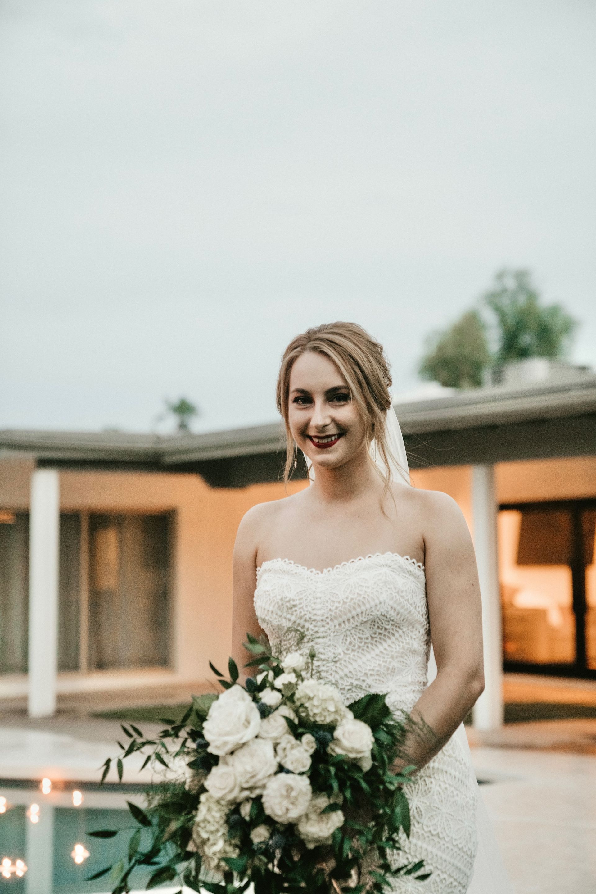 A bride in a wedding dress is holding a bouquet of flowers in front of a house.