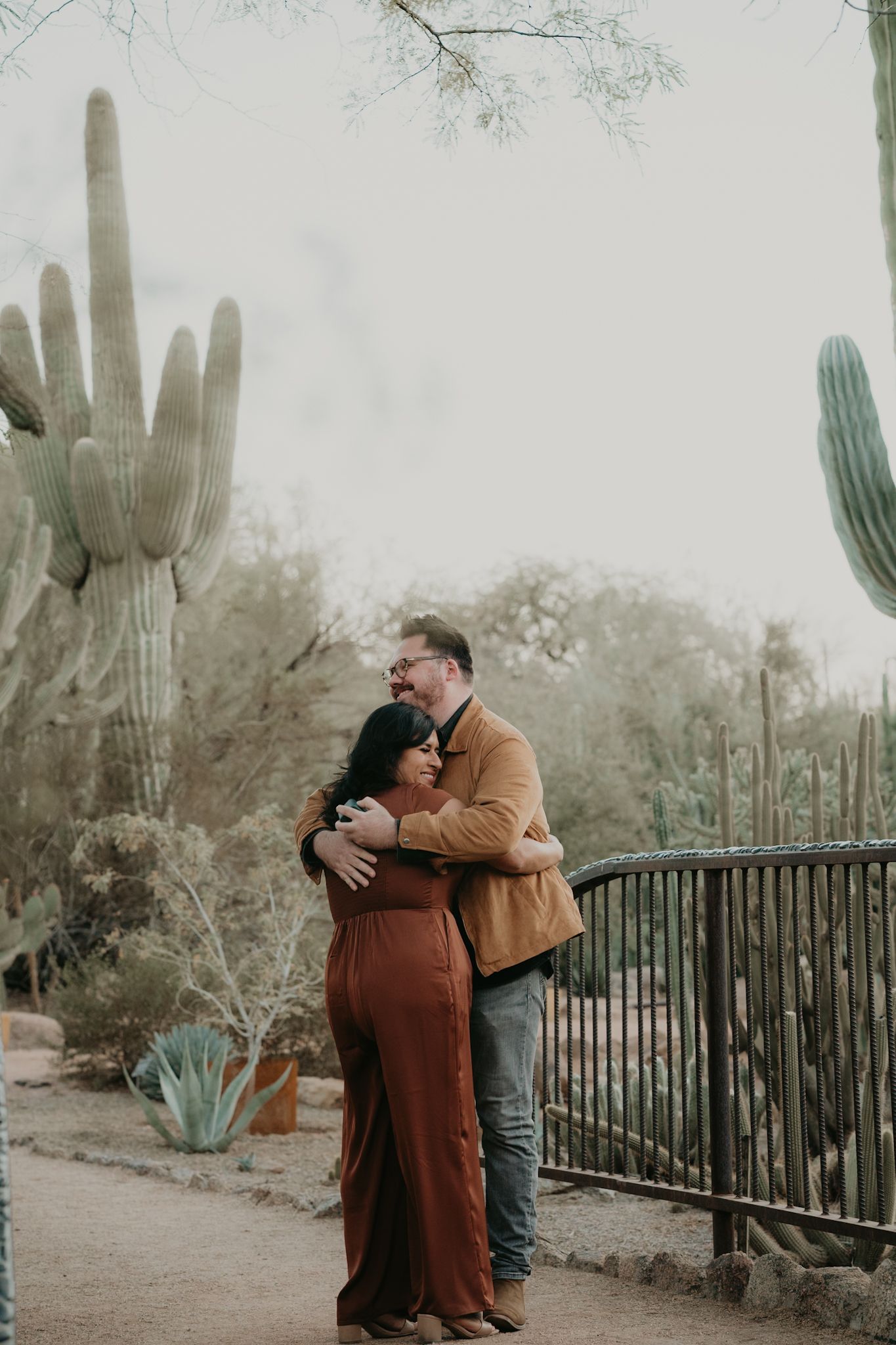 A man and a woman are hugging in front of a cactus.