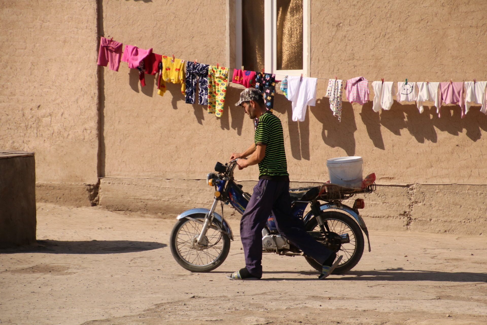 man met bromfiets loopt langs wasgoed in Khiva