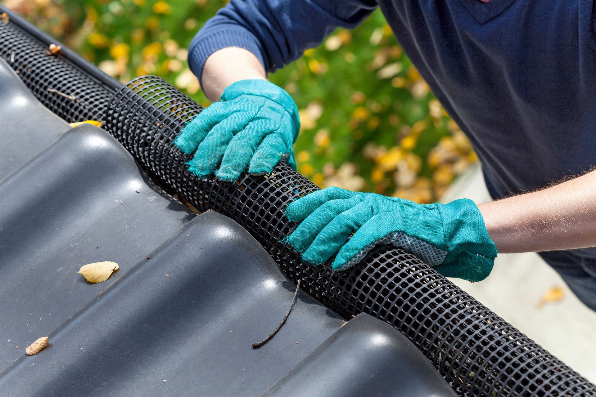 Man's hands in gloves securing gutters with black net in Chesapeake, VA.