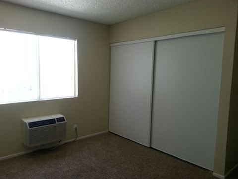Empty beige room with window, wall AC unit, and closed sliding closet doors