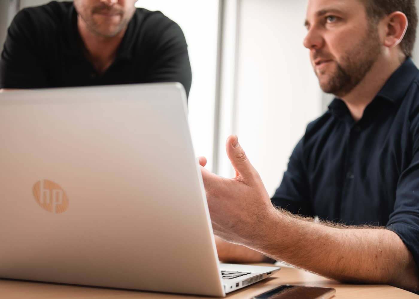 Two men are sitting at a table looking at a laptop.