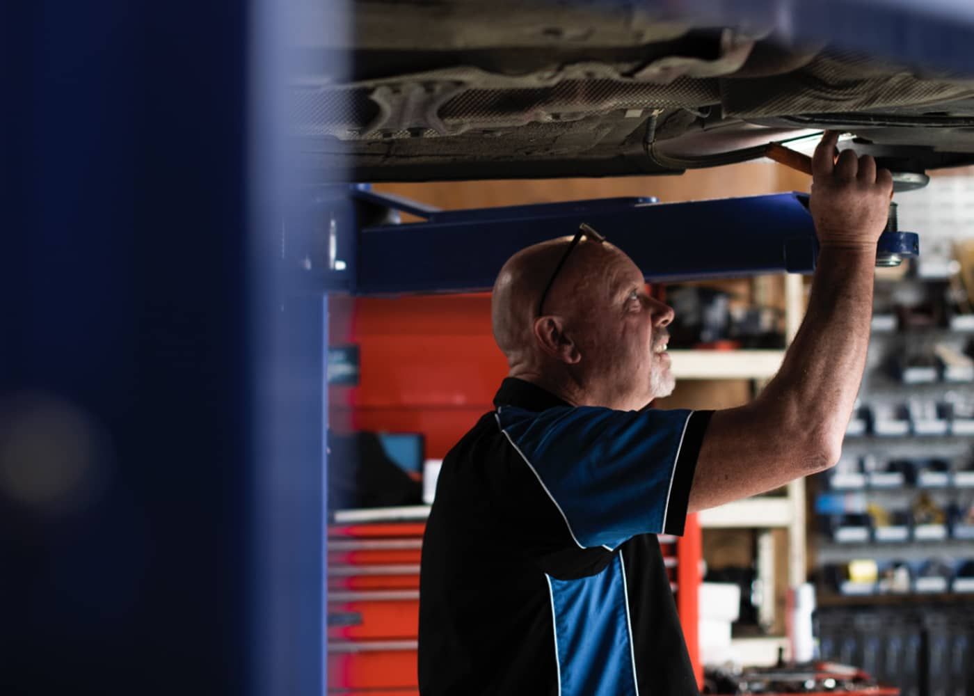 A man is working under a car on a lift in a garage.