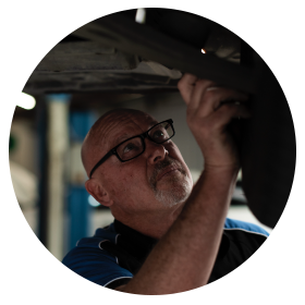 A man wearing glasses is working under a car