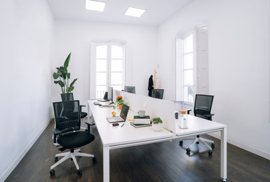Office space with white desks, black chairs, and natural light from large windows.