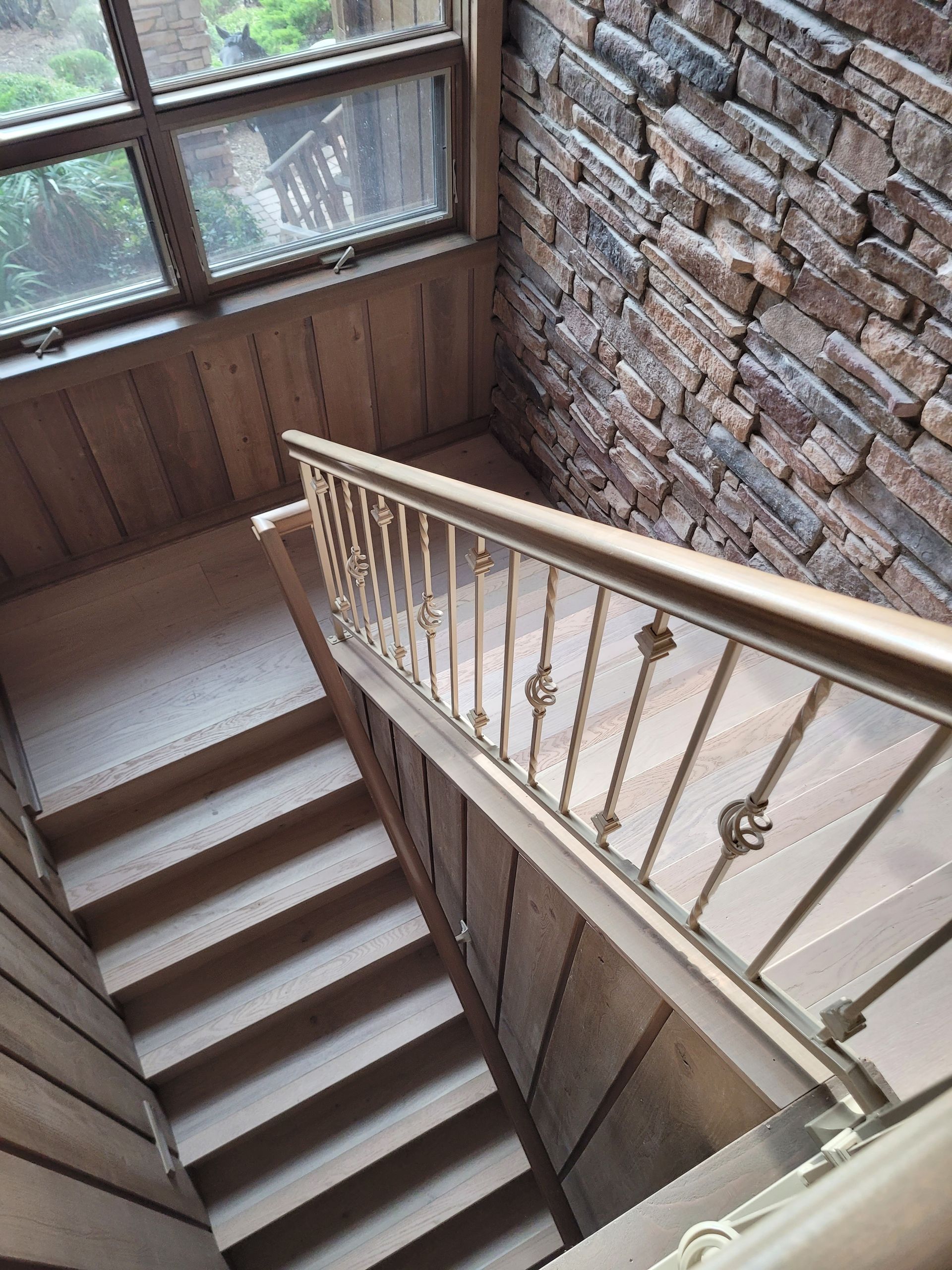 Staircase with wooden railings beside a brick wall and large window.