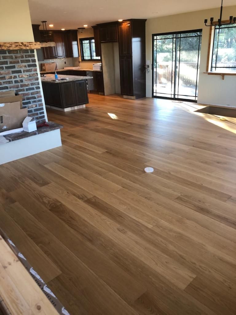 Empty living room with hardwood floors, brick fireplace, and large sliding glass doors with sunlight.