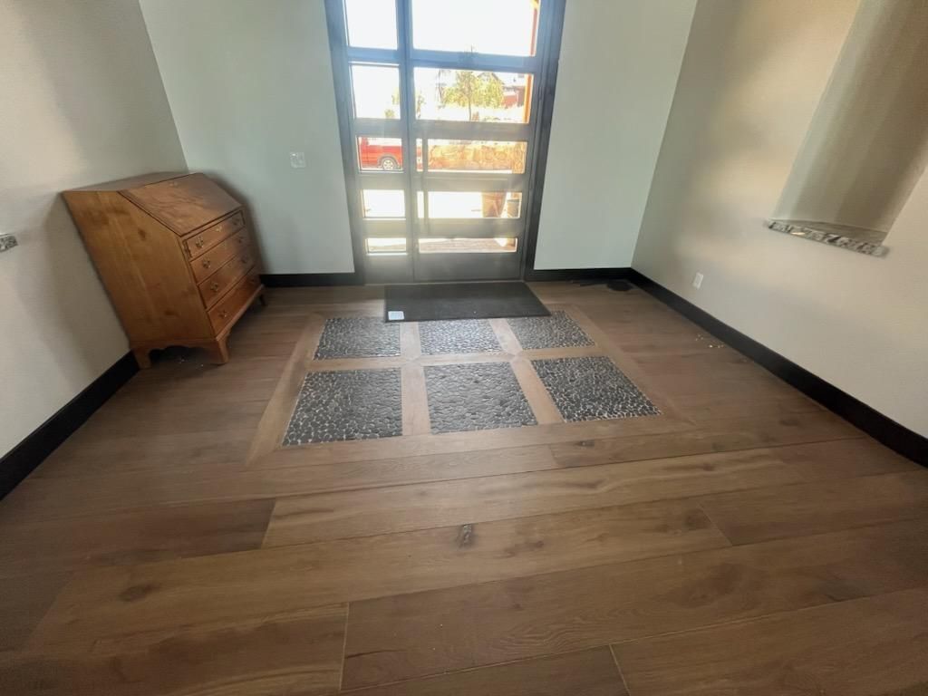 Small room with wooden floor, glass door, woven storage chest, and a patterned rug near the entrance.