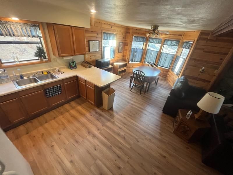 Open-plan kitchen and living room with wood floors, large windows, and a small dining table.