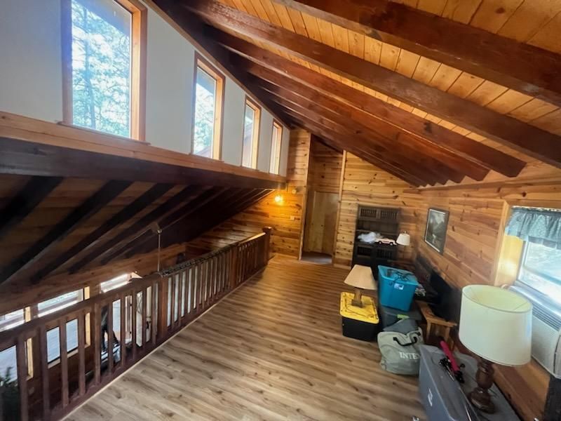 Loft interior with sloped wood ceiling, large windows, and assorted furniture and storage bins.