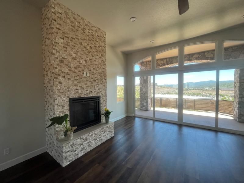 Modern living room with stone fireplace, dark wood floors, and large glass doors overlooking a scenic view