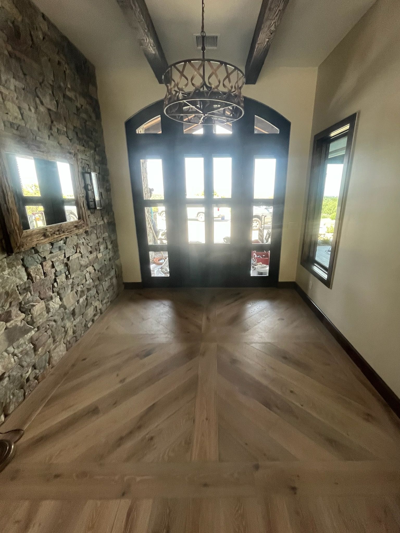 Stone-walled entry hall with wood floors, a hanging lantern, and glass double doors at the far end