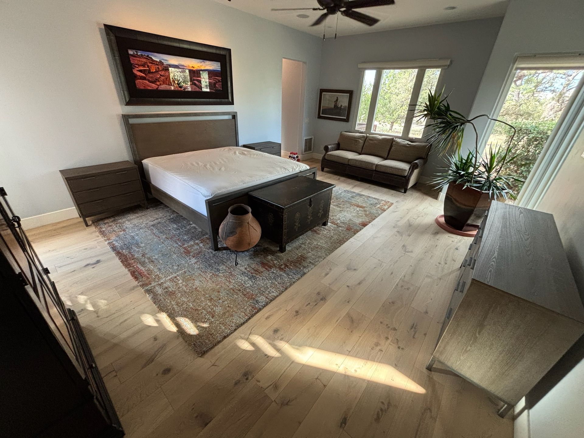 Modern bedroom with a bed, large windows, wall art, rug, and potted plants in bright sunlight