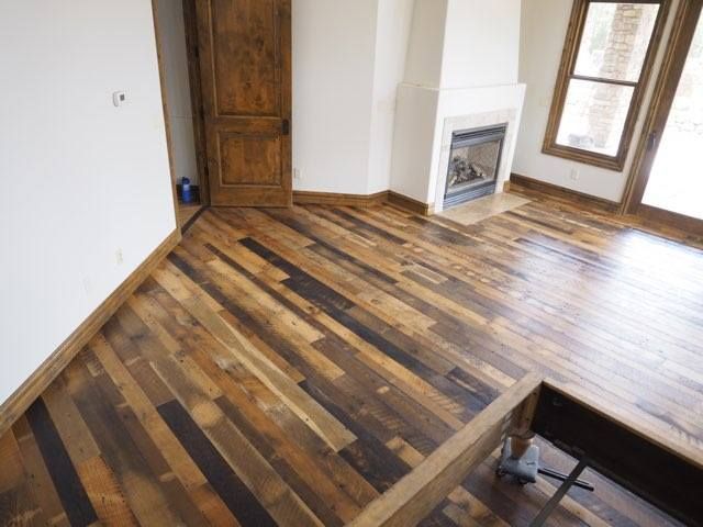 Empty room with wood plank floor, white walls, fireplace, and large windows.