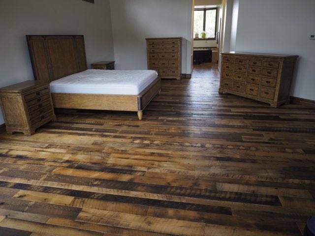 Spacious bedroom with wooden floor, bed, and two dressers near a doorway.