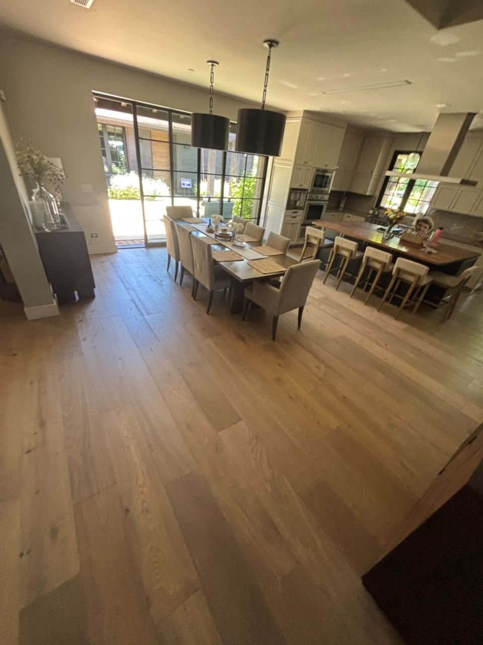 Modern dining room with long table, chairs, pendant lights, and large windows overlooking a patio.