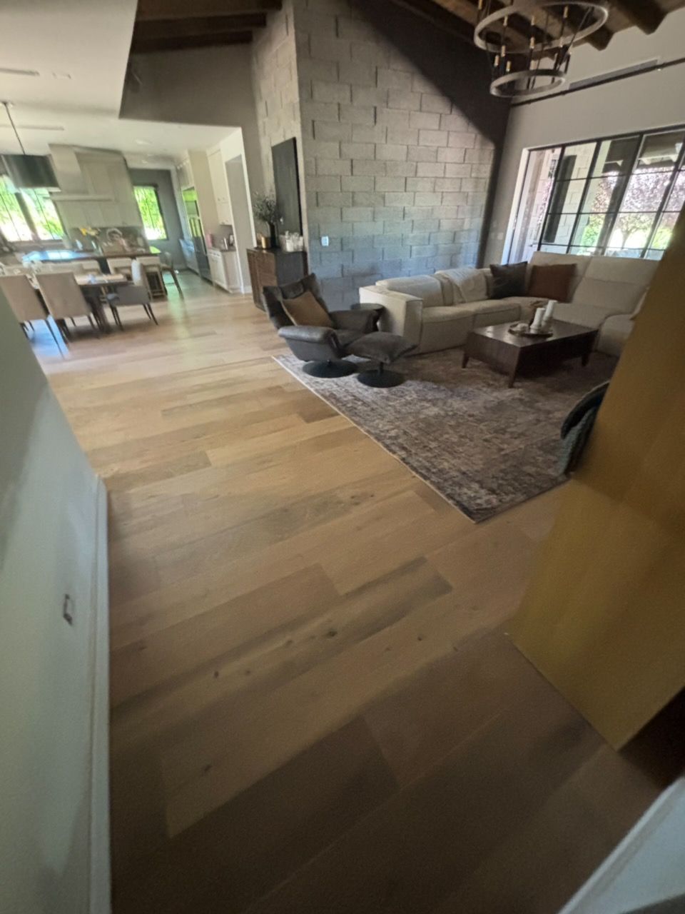 Modern living room with wood floors, gray sectional sofa, rug, and large windows in an open-plan space