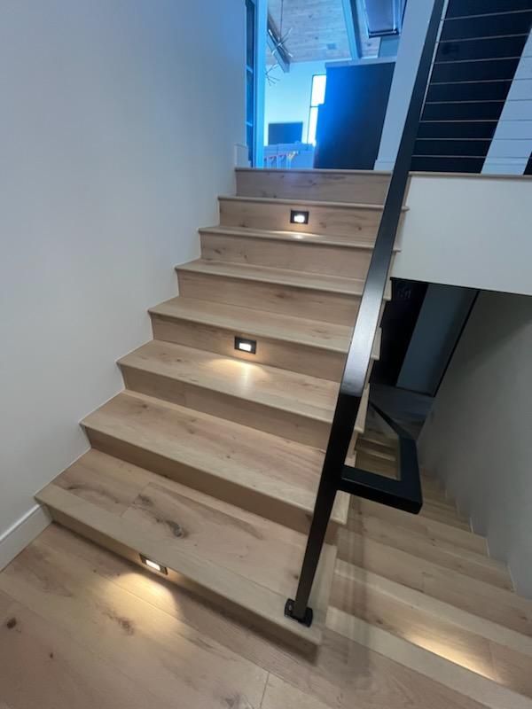 Modern wooden staircase with black railing and built-in step lights in a bright interior.