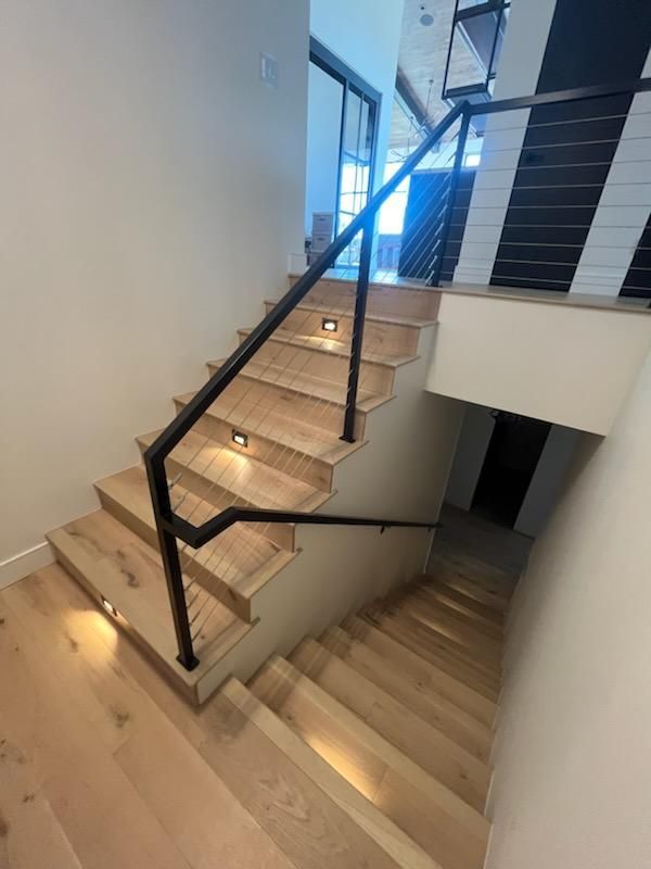 Modern indoor staircase with glass railing, wooden steps, and wall lighting in a bright home interior