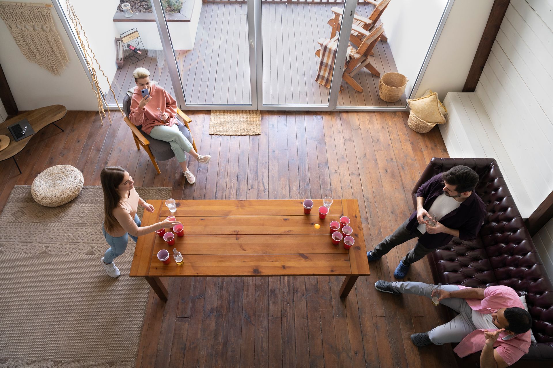 Four people gather in a high-angle view of a modern living room, playing a game at a wooden dining table.