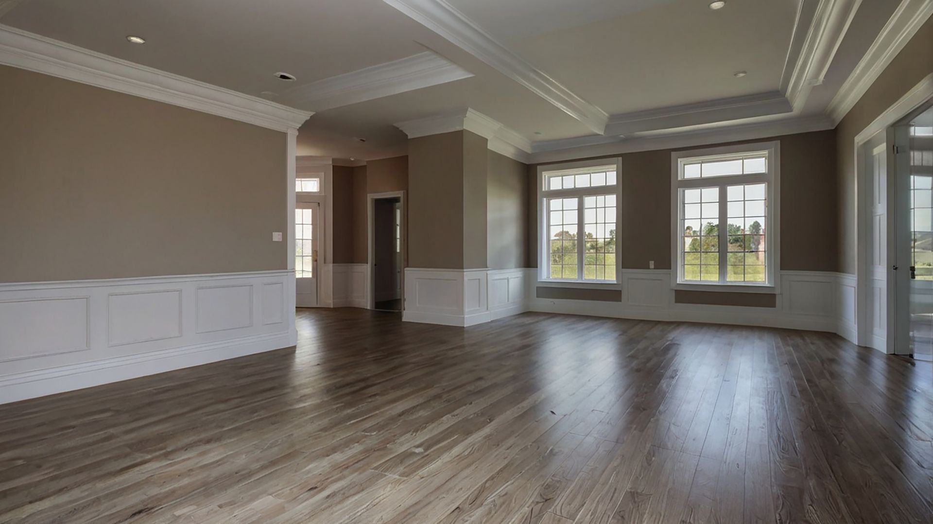 A bright, spacious room with a rustic wood floor, high vaulted ceiling, and a prominent stone fireplace wall.